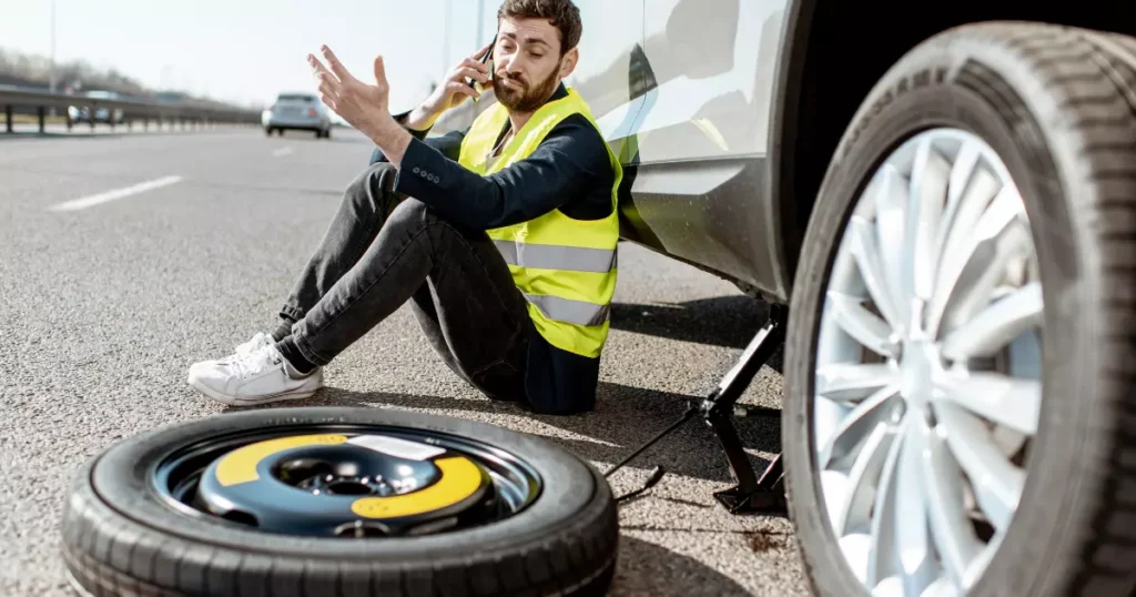 An auto repair technician sitting on the ground next to a tire